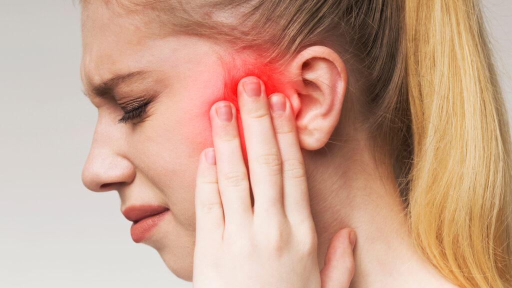Young woman has sore ear, suffering from otitis, touching her inflamed head, close up